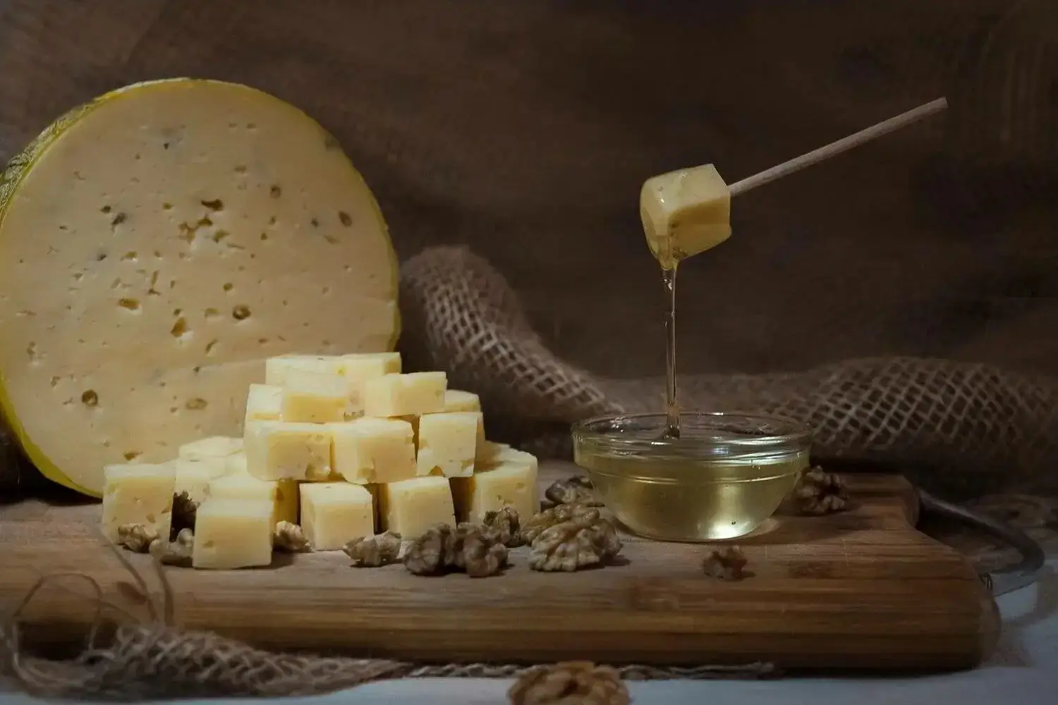 A beautiful platter of assorted cheeses, nuts, and a jar of honey.